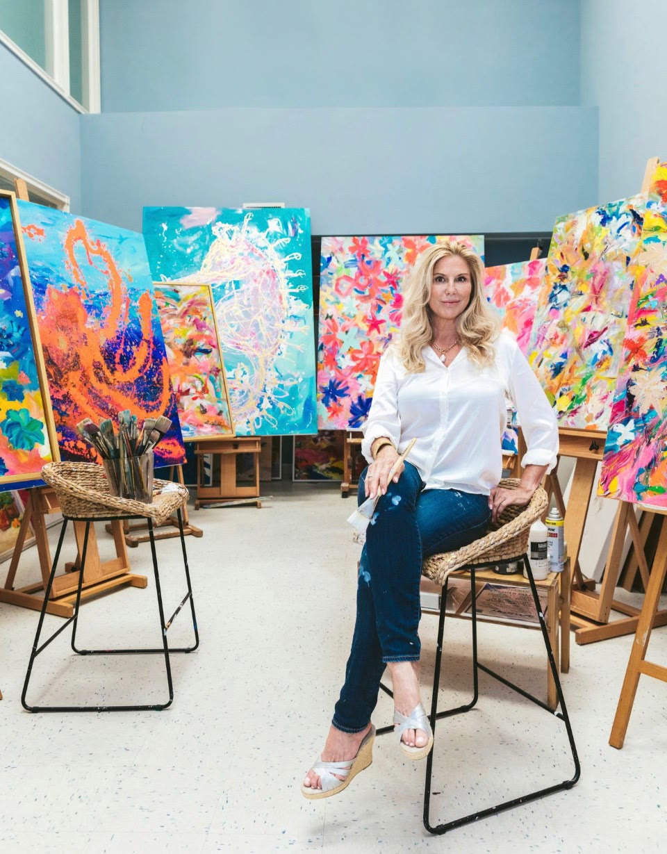 Carol seated in her studio surrounded by paintings